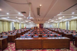 A conference room with rows of tables and chairs, a podium, and a projector. - Hua Xin Hotel Hengyang (Hengyang)