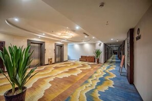 A hotel hallway with a patterned carpet, potted plants, and a reception desk. - Hua Xin Hotel Hengyang (Hengyang)