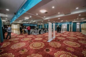 Un salón espacioso con alfombra estampada, techo alto y un grupo de personas reunidas alrededor de una estructura blanca central.