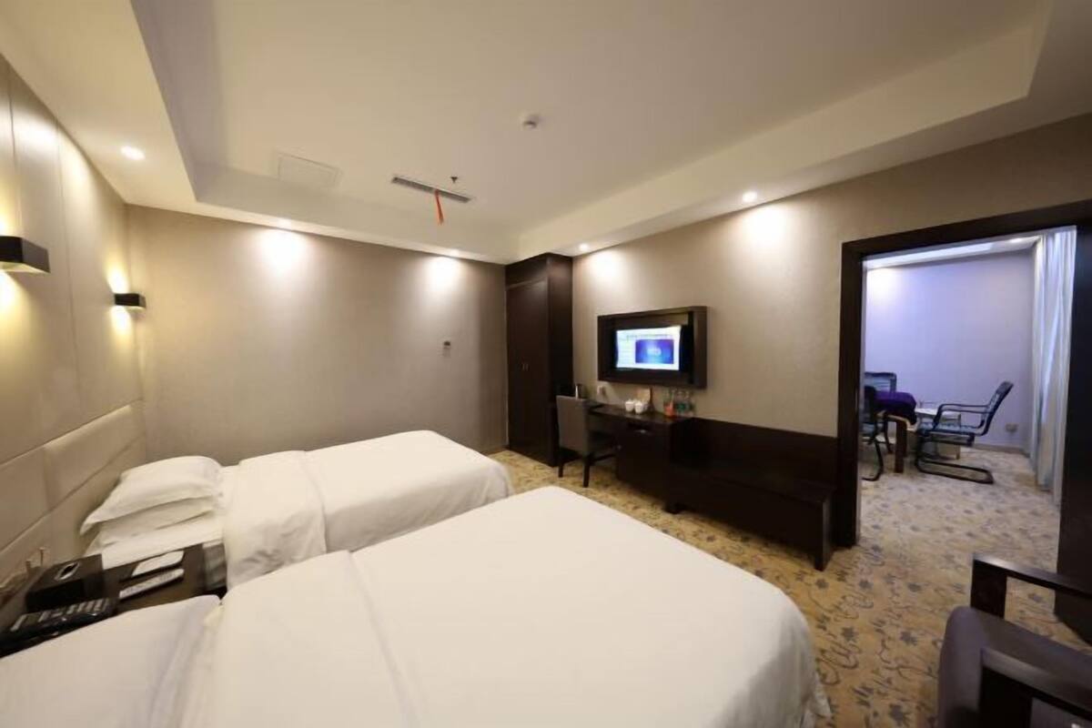 A hotel room with two beds, a desk, a television, and a chair.