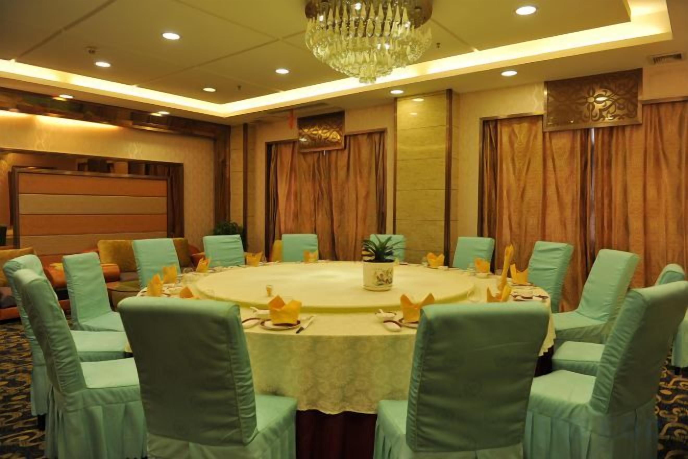 A conference room with a round table, green upholstered chairs, and a chandelier.