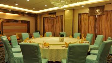 A conference room with a round table, green upholstered chairs, and a chandelier.