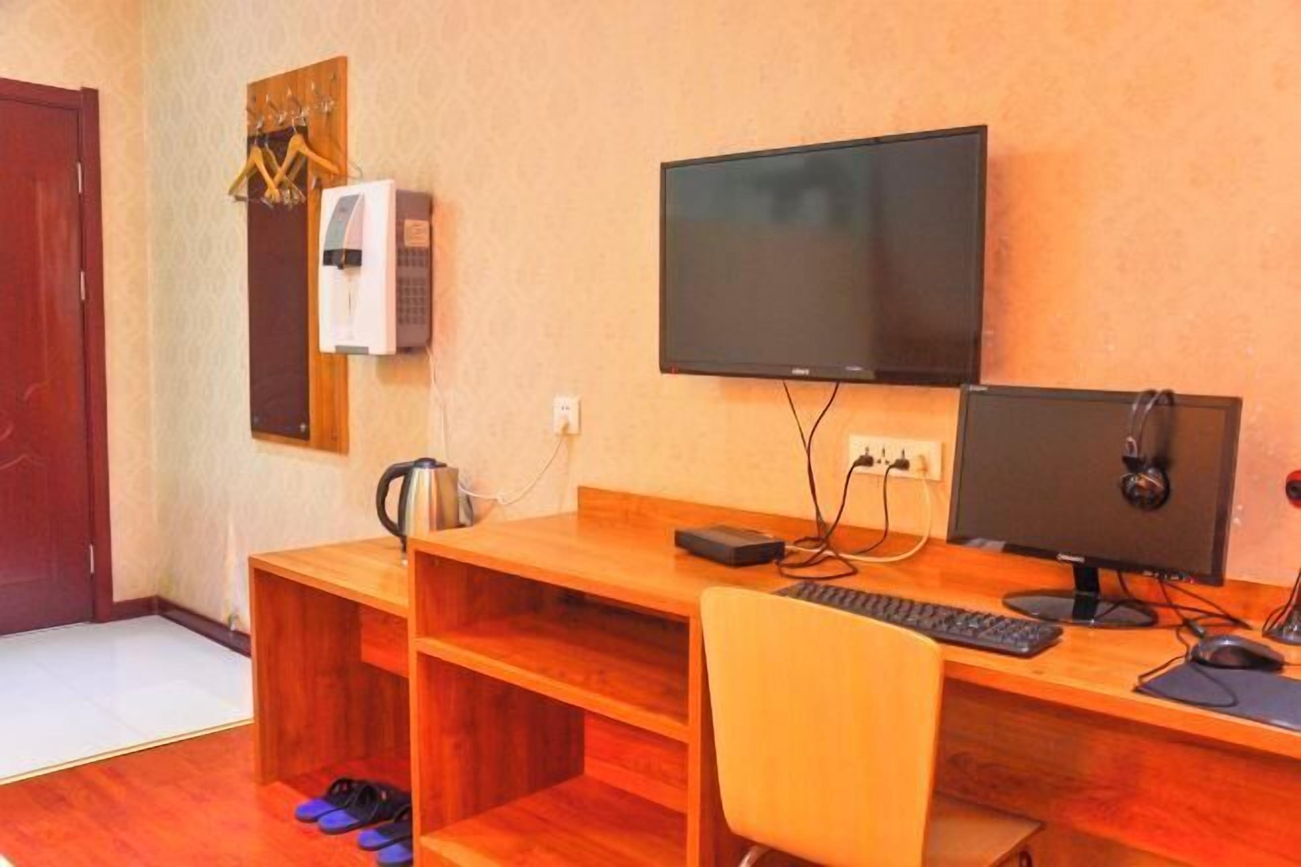 A room with a wooden desk, two monitors, a keyboard, and a chair.