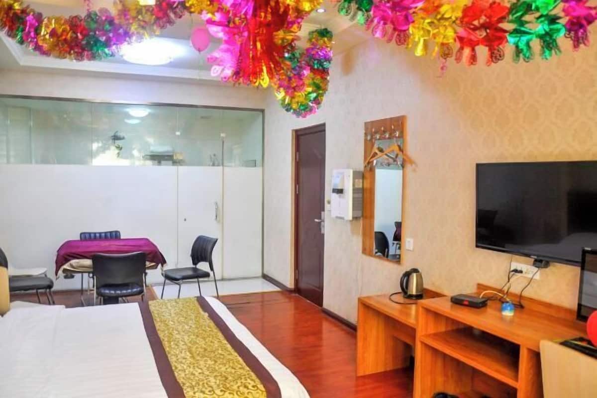 Habitación de hotel con cama, escritorio, televisor y espejo. Se ve otra habitación desde la ventana.