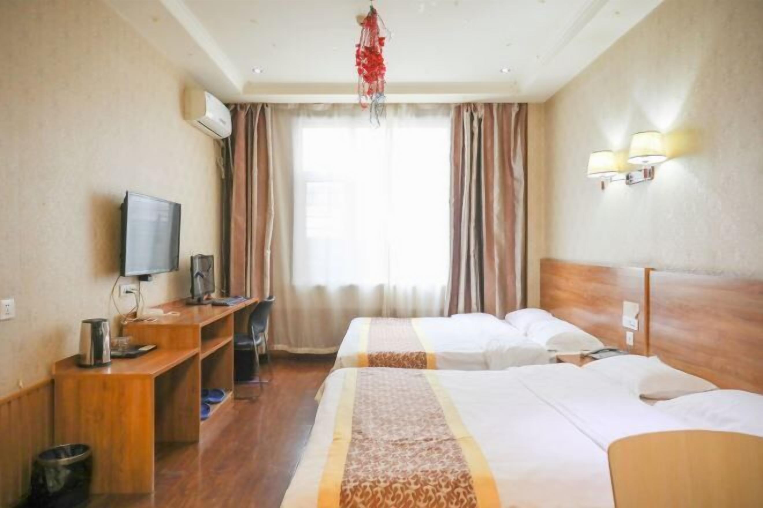 A hotel room with two beds, a desk with a television, a coffee maker, and a small trash bin.