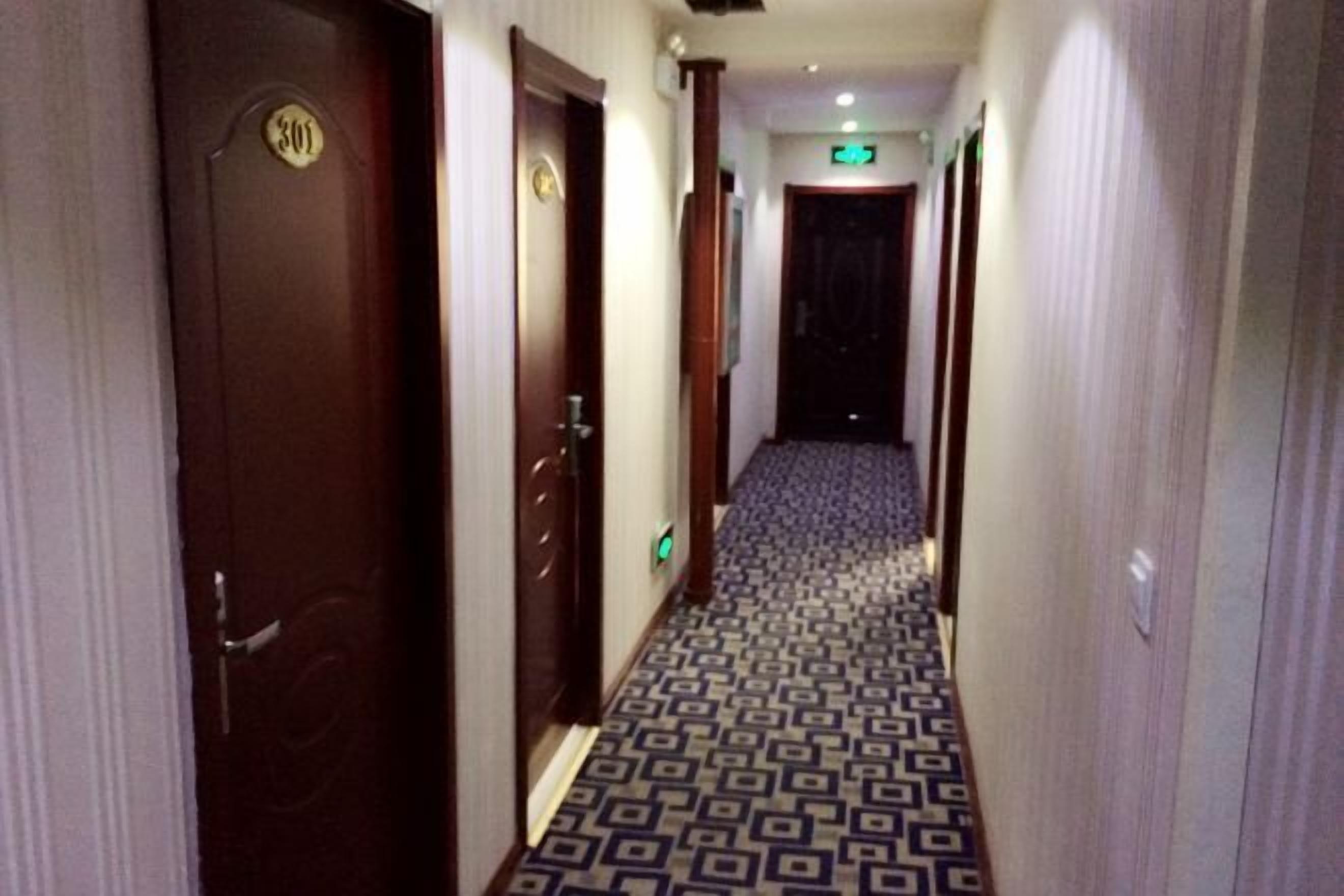 A hotel hallway with patterned carpet, wooden doors, and an exit sign.