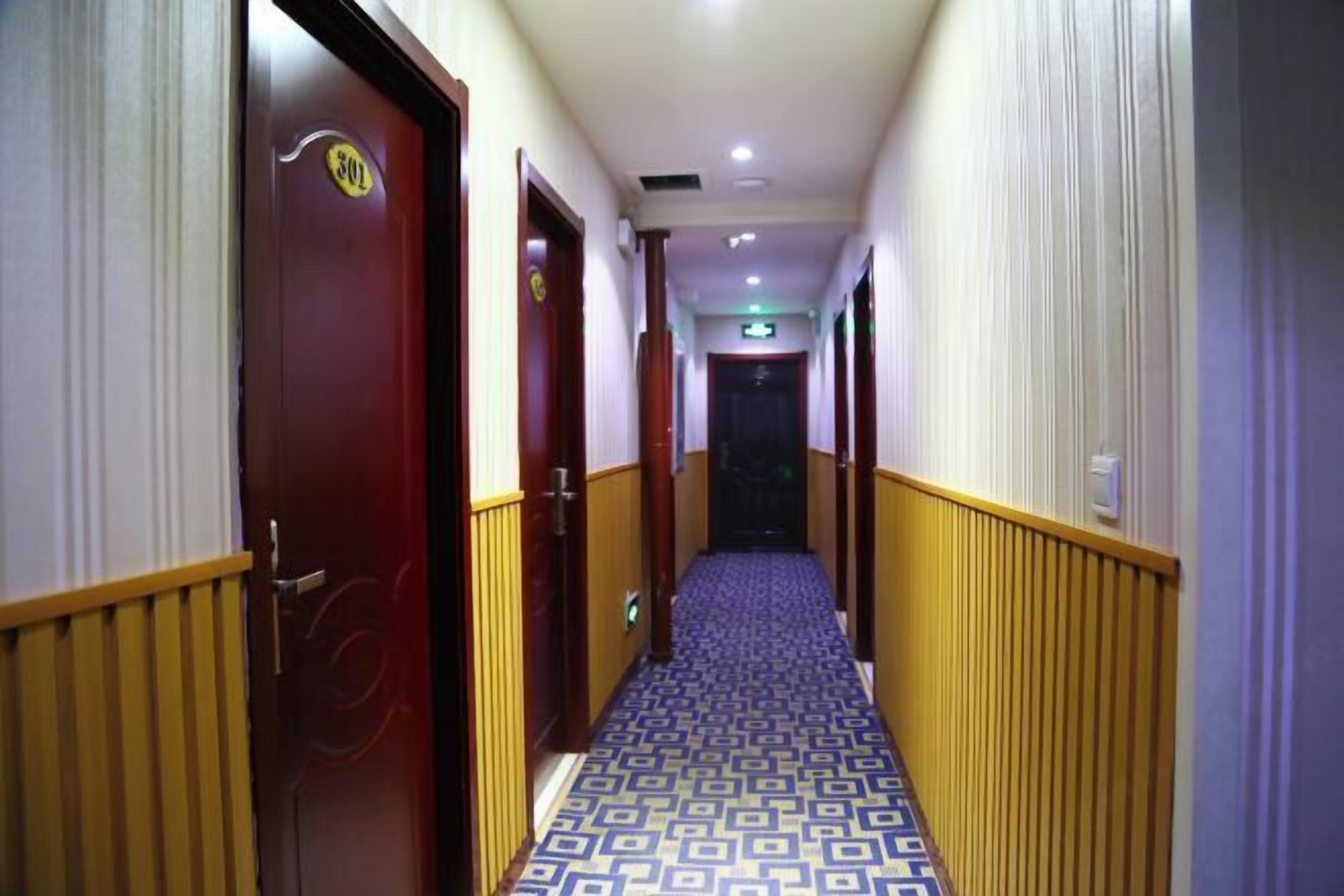 Un couloir d’hôtel avec un tapis à motifs, des lambris en bois et des portes portant les numéros des chambres.