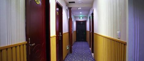 Un couloir d’hôtel avec un tapis à motifs, des lambris en bois et des portes portant les numéros des chambres.