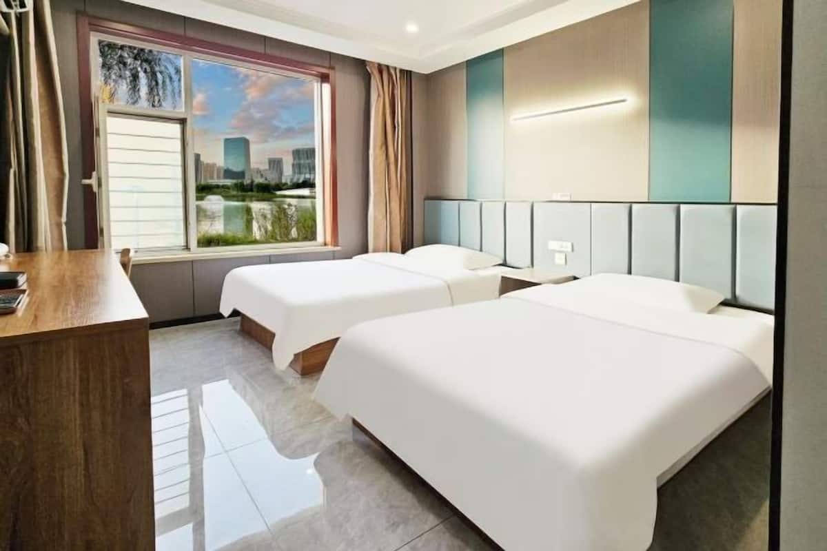 Habitación de hotel con dos camas, un escritorio y un amplio ventanal con vistas a la ciudad.