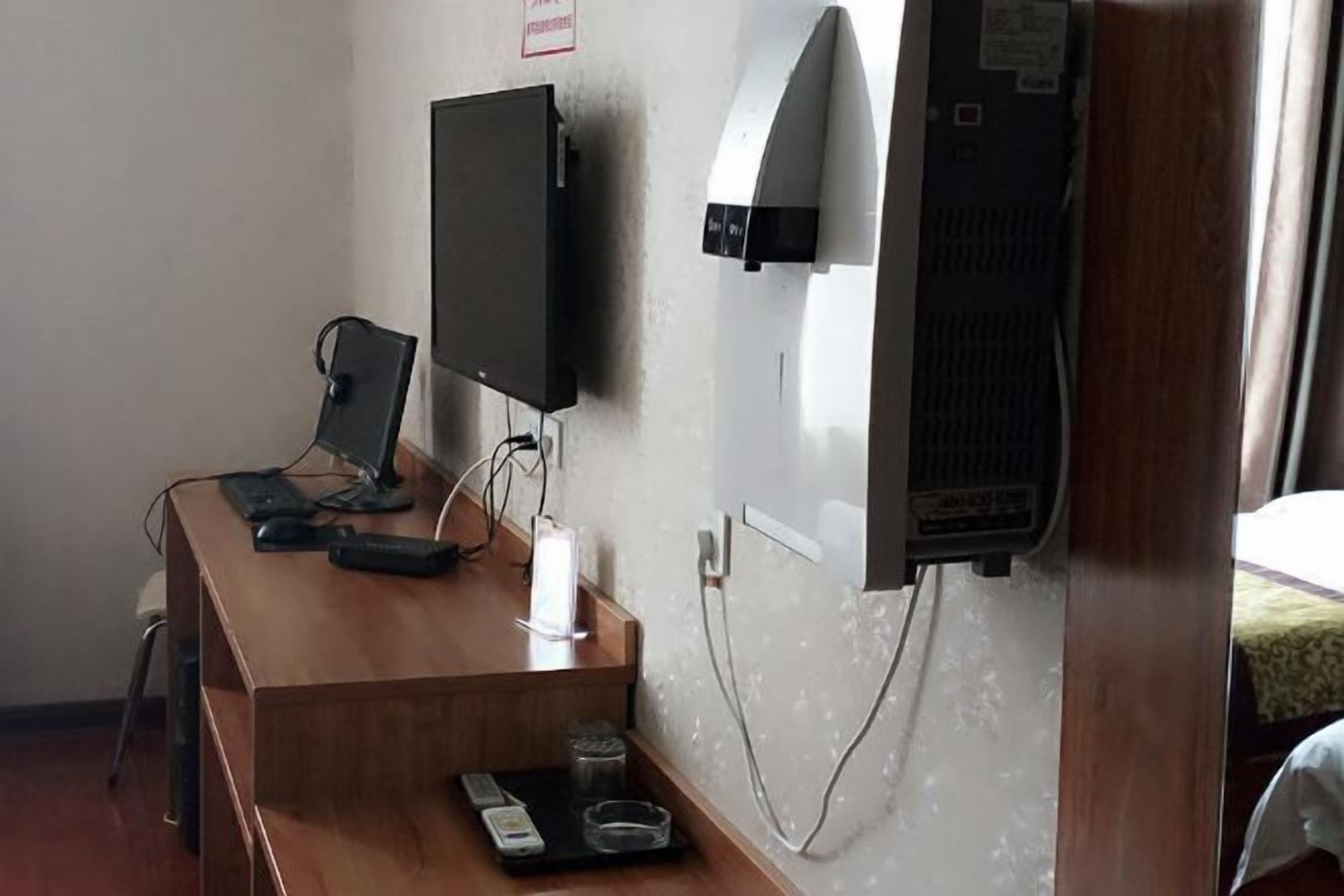 A hotel room with a wooden desk, a television, a wall-mounted air conditioner, and a power outlet.