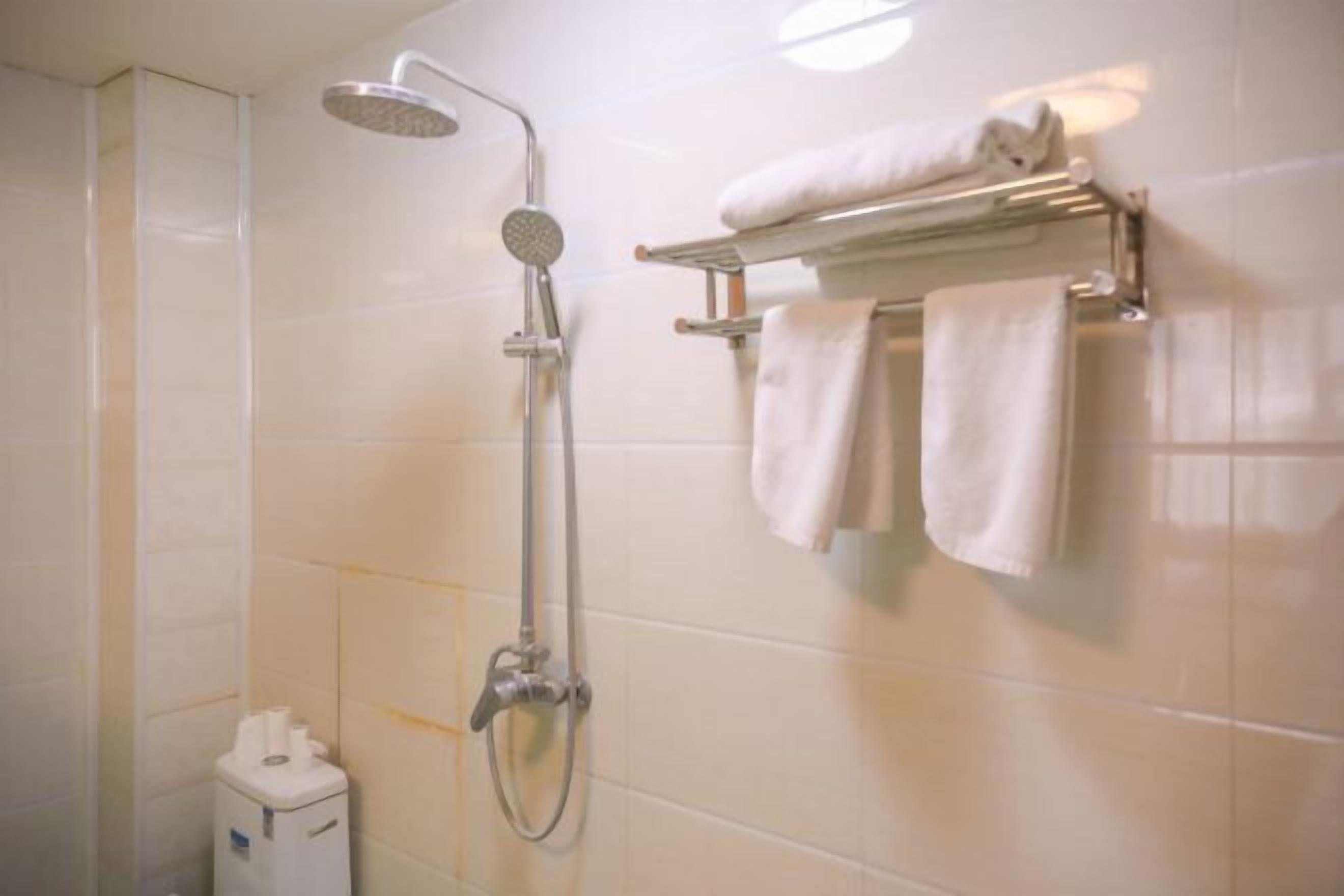 Un baño con ducha, un perchero con toallas y un dispensador de papel higiénico.