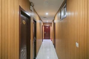 Un couloir aux murs lambrissés, avec des portes portant les numéros des chambres et un sol carrelé.