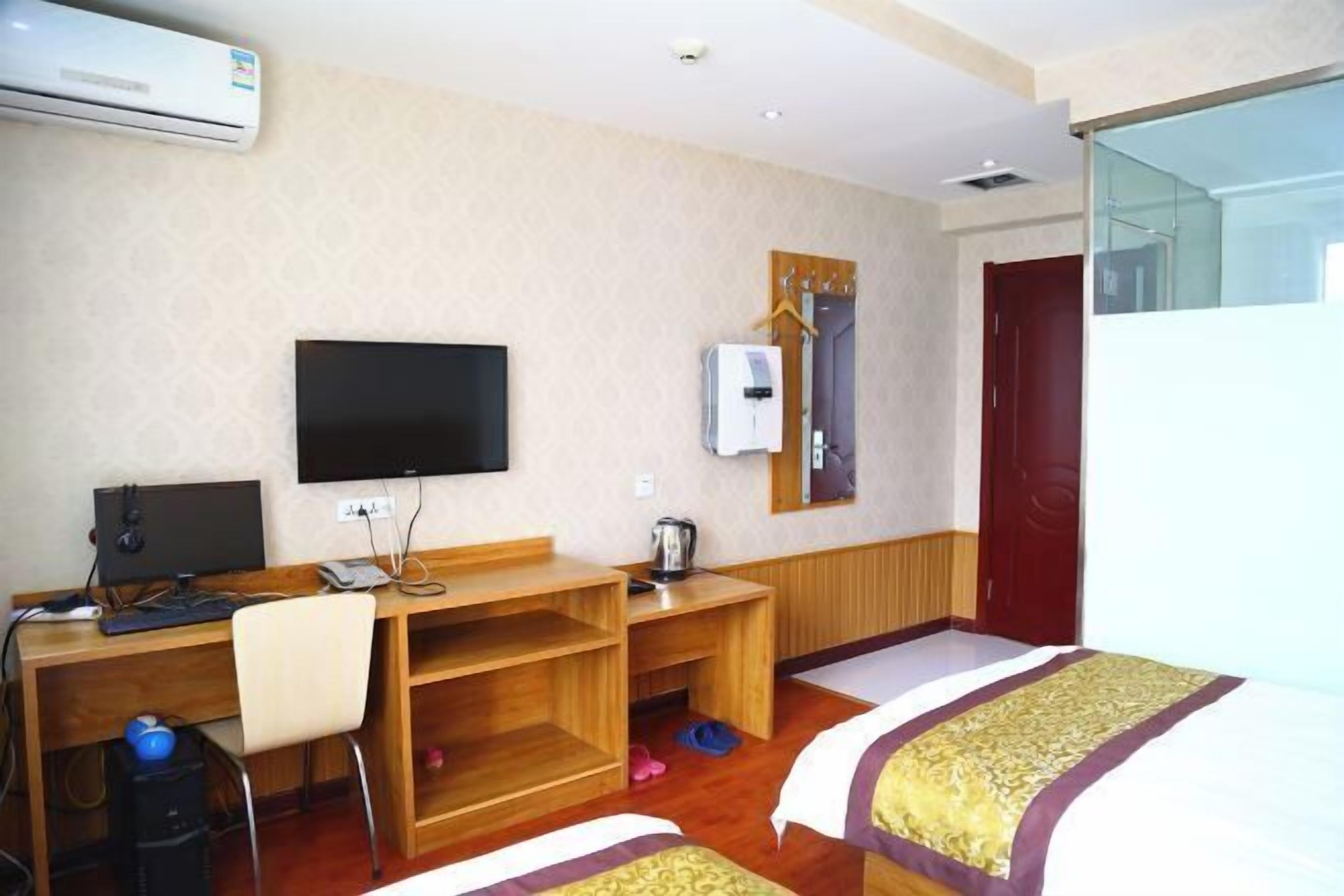 Una habitación de hotel con cama, escritorio, computadora, televisor y aire acondicionado.
