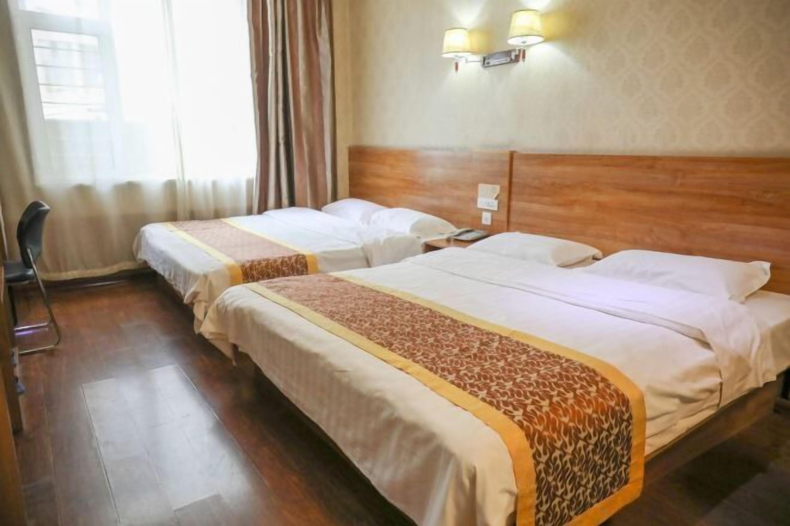 A hotel room with two single beds, wooden headboards, a small desk, and a chair.