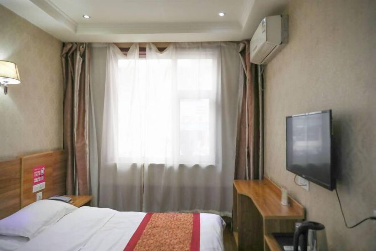 Una habitación de hotel con una cama, un escritorio, un televisor y una ventana con cortinas.