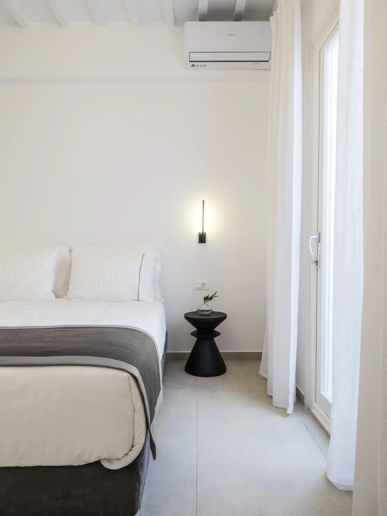 Une chambre à coucher au style minimaliste, avec un lit, une table de chevet et une lampe fixée au mur.
