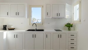 A modern kitchen with white cabinets, a black faucet, and a window with a view of buildings. - Sunset Windmills Houses (Mykonos)