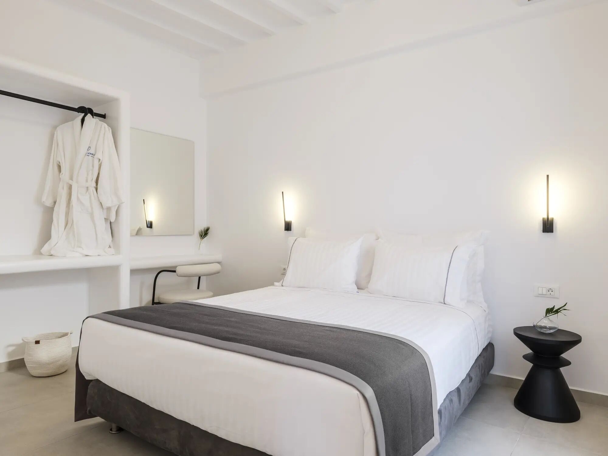 A modern bedroom with a large bed, bedside tables, a robe rack, and a mirror.