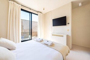 Quarto de hotel com cama, televisão fixada na parede e varanda com grade.