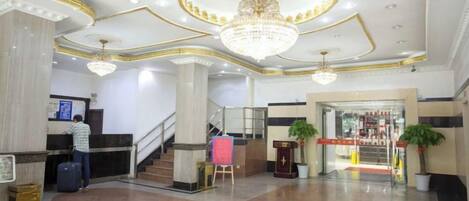 A hotel lobby with a reception desk, a staircase, and a large chandelier.