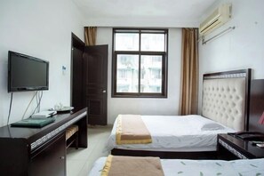 Habitación de hotel con cama, escritorio con computadora, televisión y ventana con cortinas.