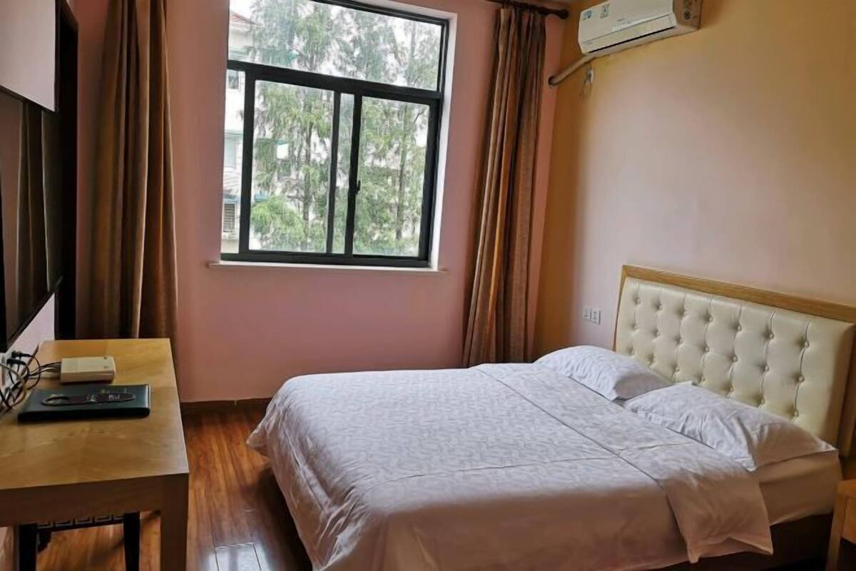 Quarto com cama, janela, mesa e um laptop, além de ar condicionado.