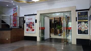 A hotel lobby with a reception desk, a staircase, and a glass door leading to a restaurant.