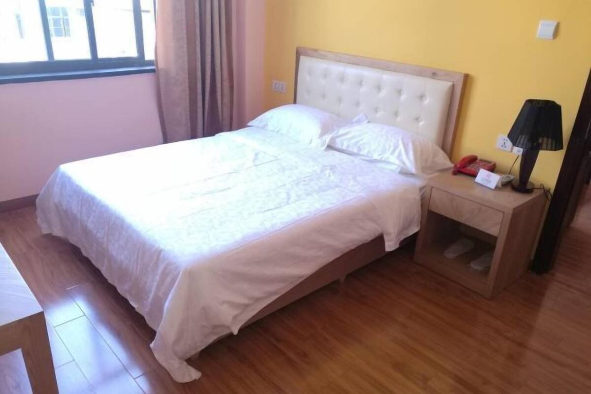 Uma cama com cabeceira de madeira, mesa de cabeceira com abajur e janela com cortinas.