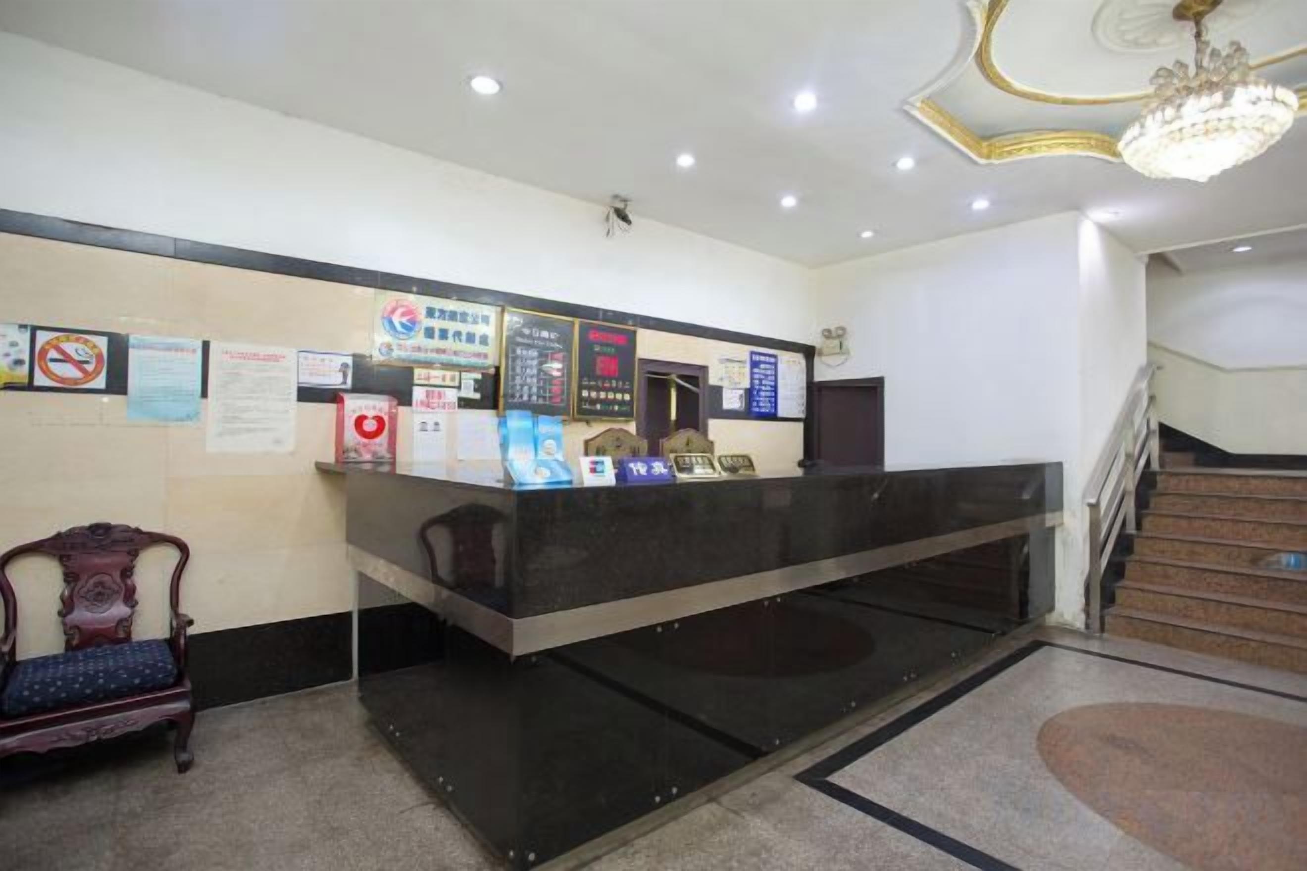 A reception desk with a black counter, a chandelier, and a staircase in the background.