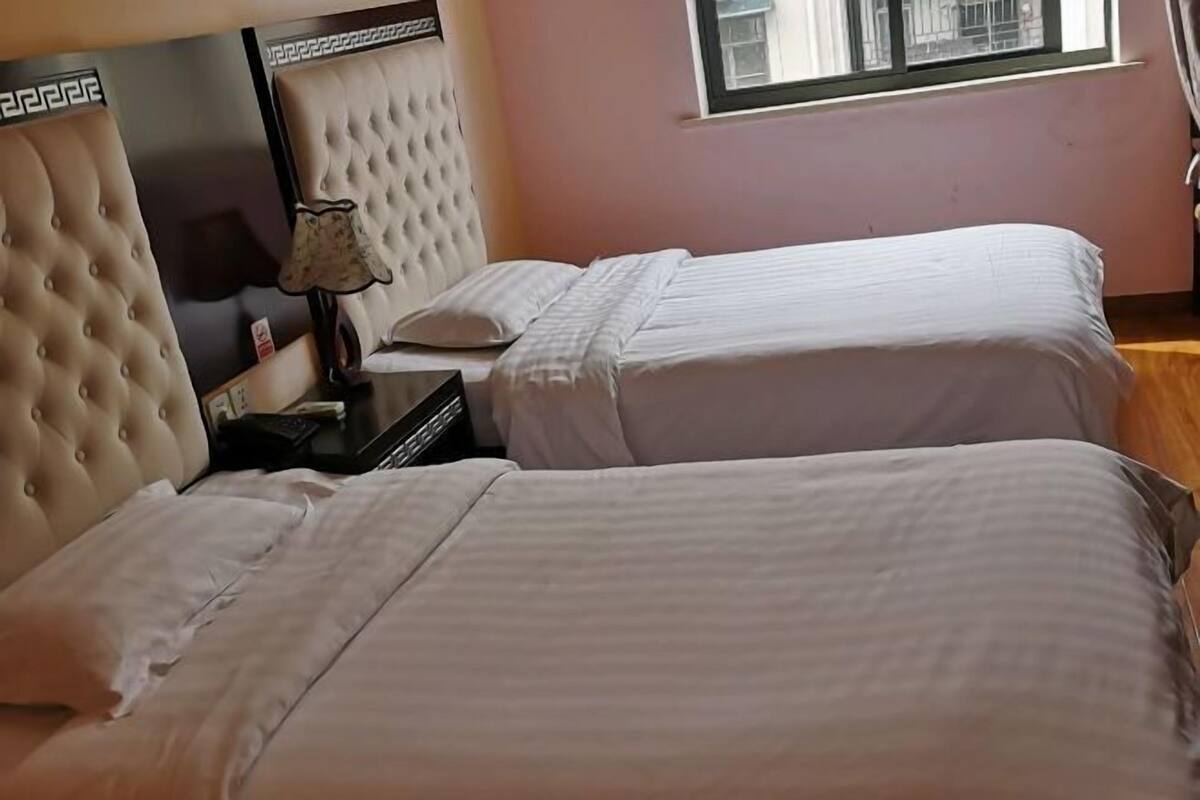 Quarto de hotel com duas camas, uma mesa de cabeceira, um abajur e uma janela com cortinas.