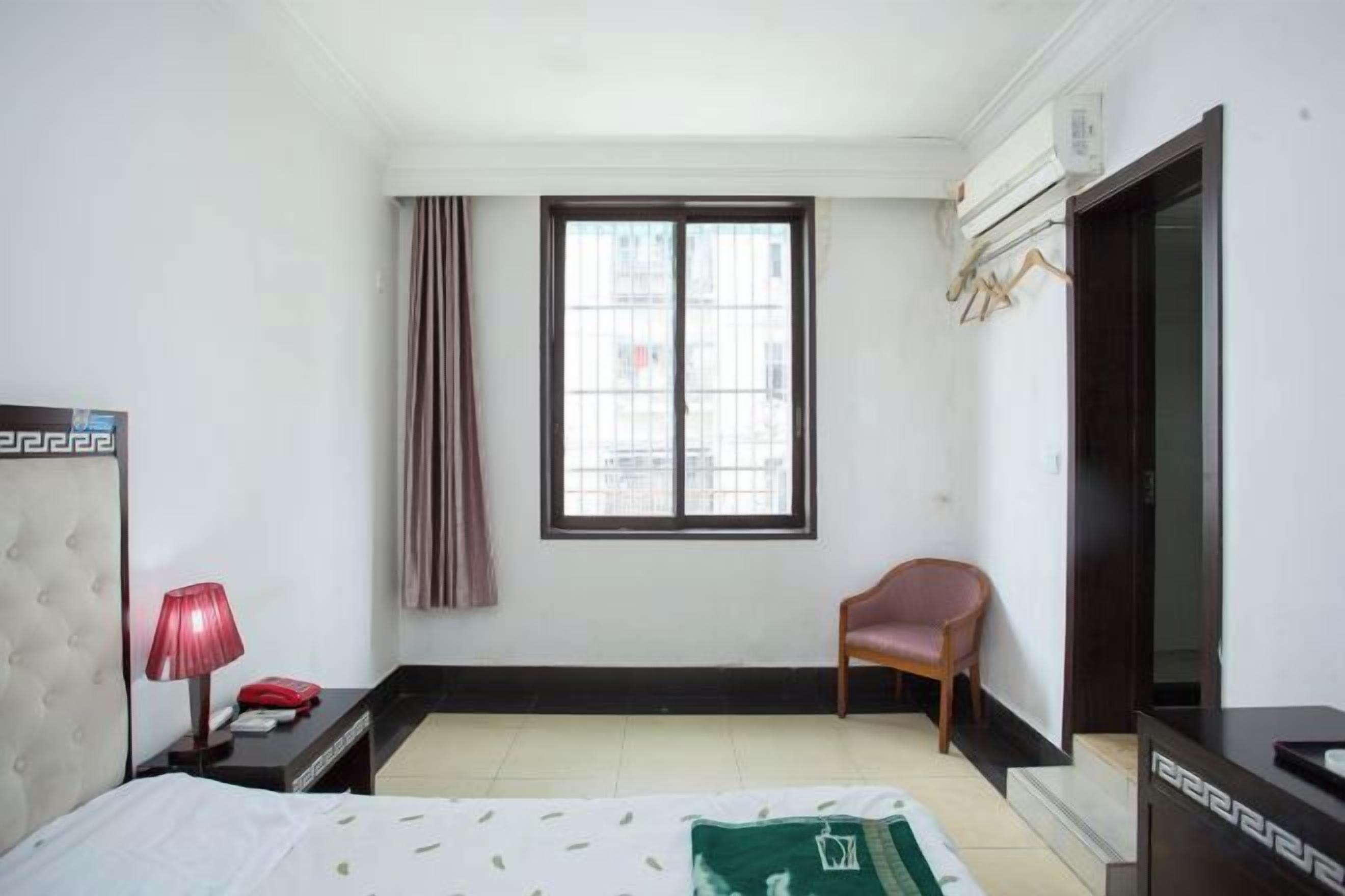 A hotel room with a bed, a chair, a desk, a TV, and a window with curtains.