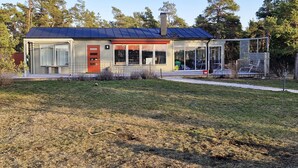A modern house with a red door, large windows, and a solar panel roof.