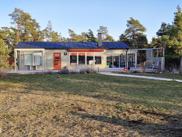 A modern house with a red door, large windows, and a solar panel roof.