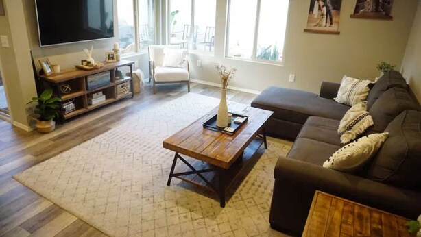 A living room with a large flat-screen TV, a wooden coffee table, a brown sofa, and a white armchair.