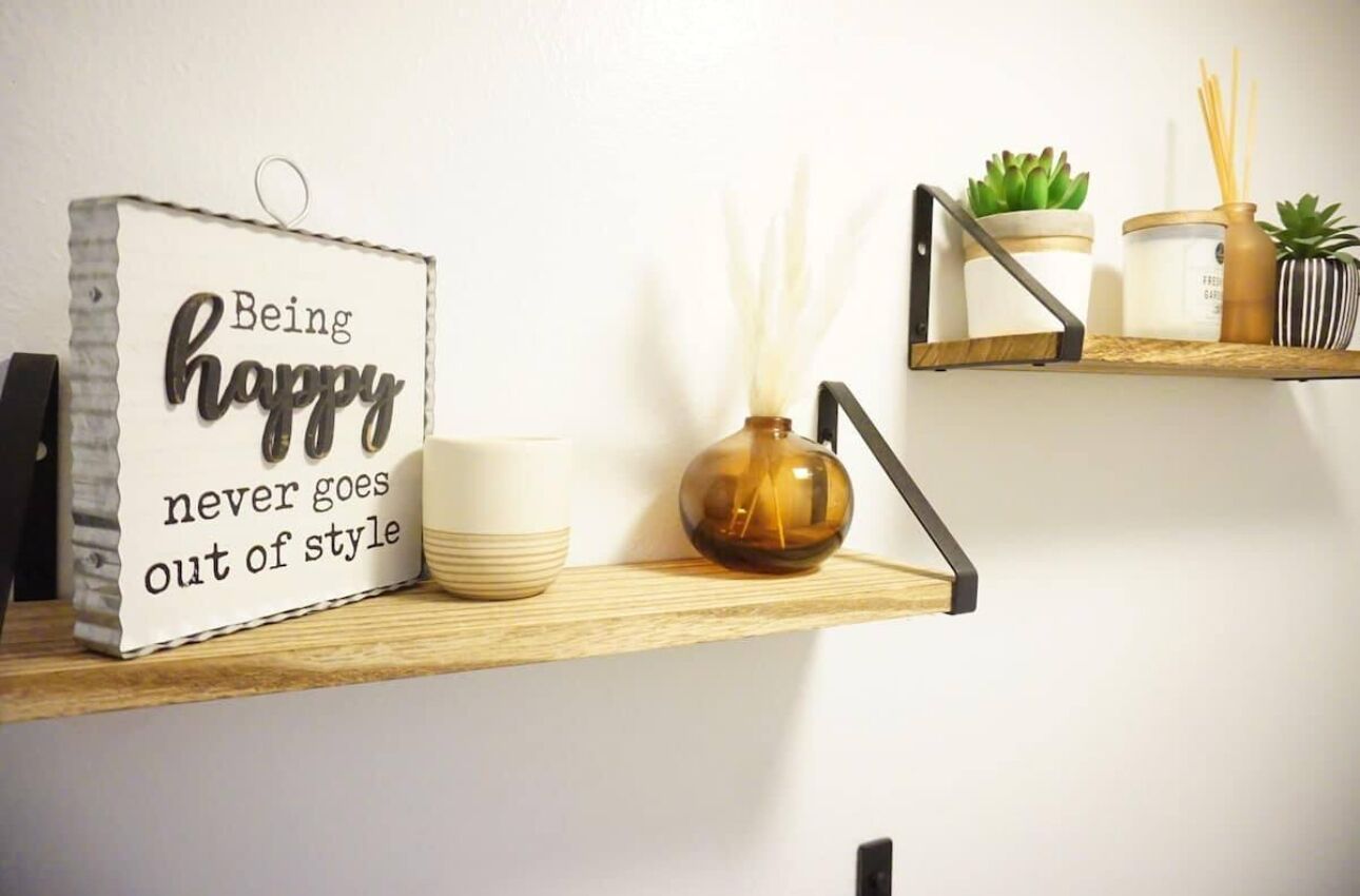 A shelf with a sign saying "Being happy never goes out of style," a white vase, and a small succulent plant.