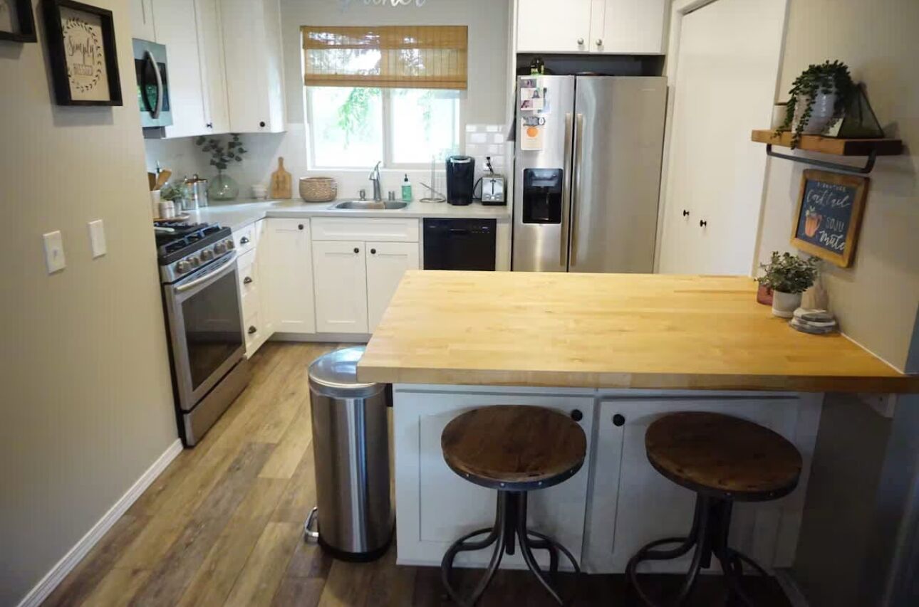 A kitchen with white cabinets, a wooden countertop, a stainless steel refrigerator, and two stools.