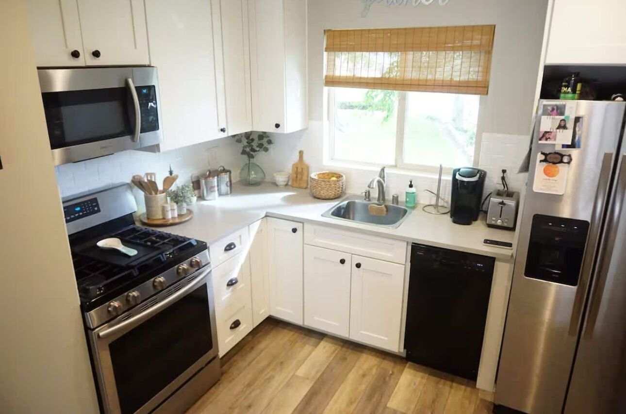 A compact kitchen with white cabinets, a stainless steel microwave, a stove, a dishwasher, and a refrigerator.