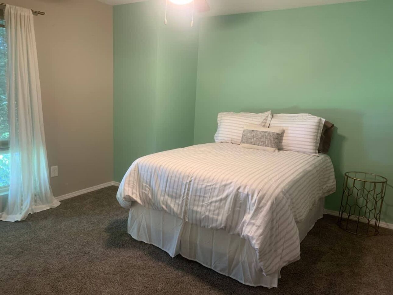Une chambre avec un lit, une fenêtre ornée d’un rideau léger et une petite table ronde.