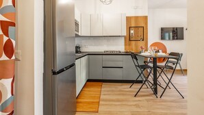 A modern kitchen with a stainless steel refrigerator, grey cabinets, a wooden accent wall, a dining table with chairs, and a hanging pendant light. - Domus Aqua Alexandrina by Rentbeat (Roma)