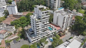 A multi-story residential building with balconies, a rooftop pool, and surrounding greenery.