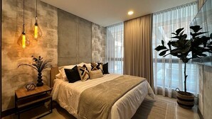 A modern bedroom with a large bed, a bedside table with a lamp, and a potted plant. - RM 210 | Beauty, Balcony, Elevator, Security, Pool (Cali)
