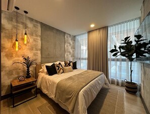 A modern bedroom with a large bed, a bedside table with a lamp, and a potted plant.
