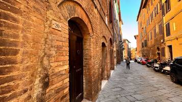 A narrow cobblestone street lined with historic brick buildings, featuring a prominent arched doorway with a number plaque.