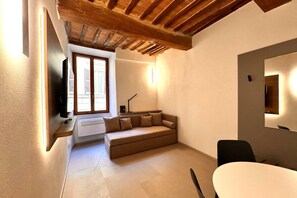 A cozy room with a sofa, a dining table, and a TV mounted on the wall.