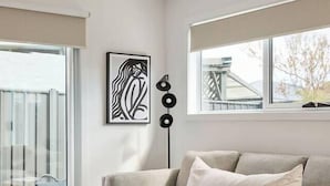 A modern living room with a grey sofa, a wooden coffee table, and a colorful rug. There is a large window with a view of a bridge and trees. - Welcome to Birch BnB (Newstead)