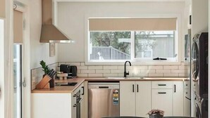 A modern kitchen with white cabinets, a wooden dining table, and a window providing natural light. - Welcome to Birch BnB (Newstead)