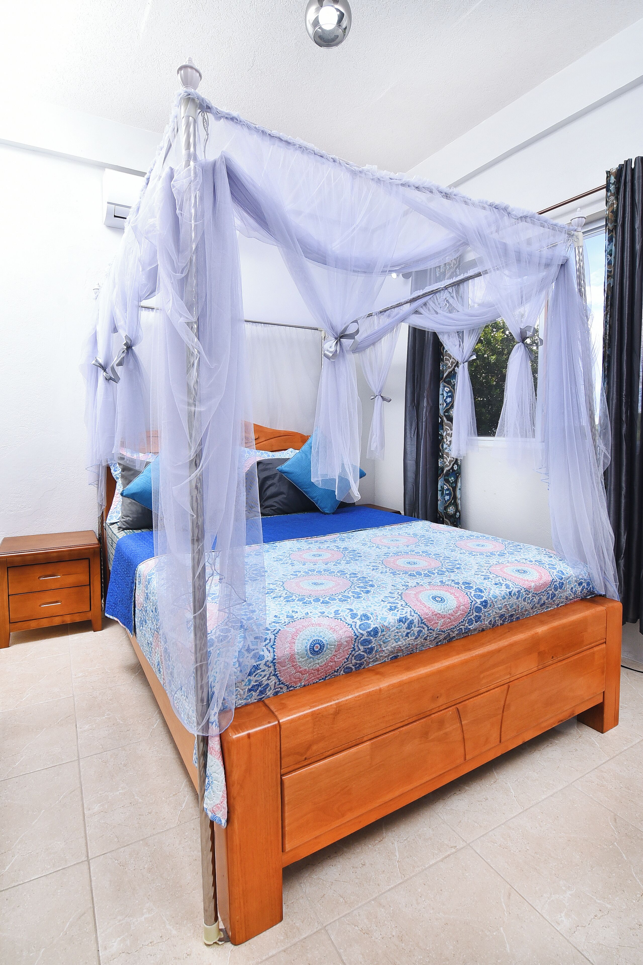 A bedroom with a wooden bed, a nightstand, and a window with curtains.