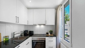 A modern kitchen with white cabinets, a black countertop, a built-in oven, and a window providing a view of the outside. - book2stay: modern Apartment at Top Place (Olma Messen) (St. Gallen)