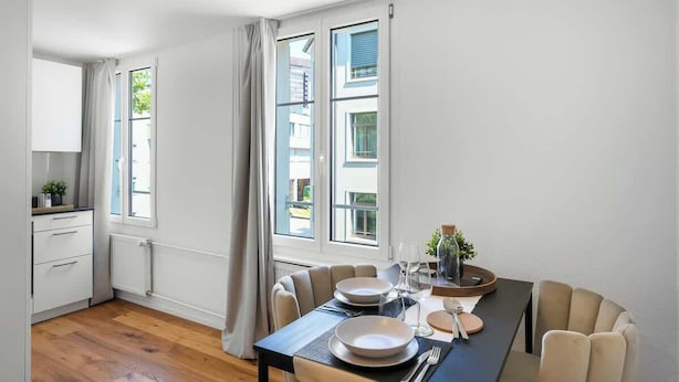 A modern dining area with a table set for two, large windows, and a view of the outside. - book2stay: modern Apartment at Top Place (Olma Messen) (St. Gallen)