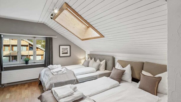 A bedroom with two beds, a skylight, a window with curtains, and a view of buildings outside. - book2stay: Retro-Alpin Studio (Laax)